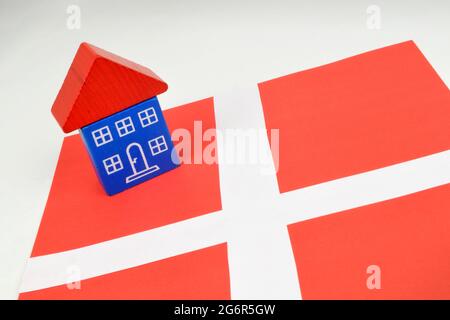 Ein Spielzeughaus, das auf einer dänischen Flagge sitzt. Ein Stillleben auf dänischem Grundstück. Stockfoto