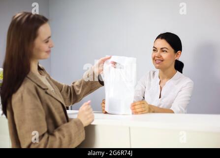 Weibliche Klientin, die eine Tasche mit Kosmetikartikeln von einem freundlichen Mitarbeiter an der Rezeption in der Kosmetikklinik mitnimmt Stockfoto