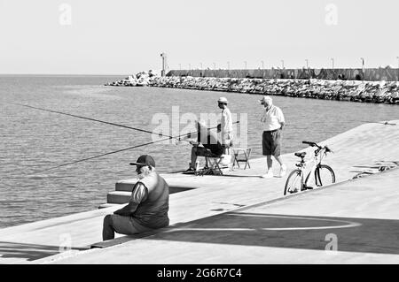 Pesaro, Italien - 9. juli 2020: Ein kleiner Junge fischt mit seinem Vater und seinem Großvater auf dem Dock des Hafens von Pesaro Stockfoto