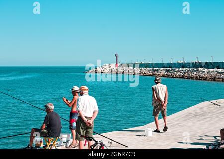 Pesaro, Italien - 9. juli 2020: Ein kleiner Junge fischt mit seinem Vater und seinem Großvater auf dem Dock des Hafens von Pesaro Stockfoto