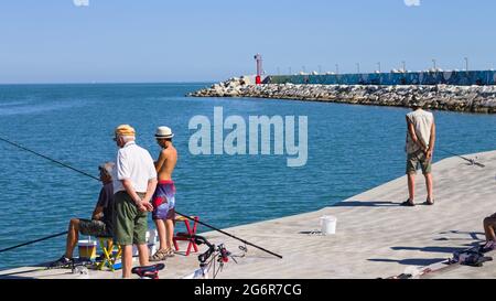 Pesaro, Italien - 9. juli 2020: Ein kleiner Junge fischt mit seinem Vater und seinem Großvater auf dem Dock des Hafens von Pesaro Stockfoto