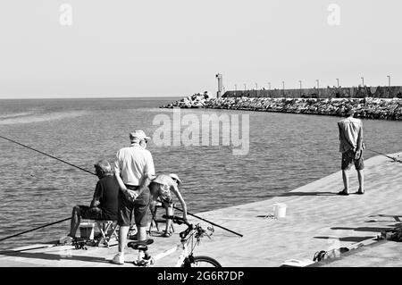 Pesaro, Italien - 9. juli 2020: Ein kleiner Junge fischt mit seinem Vater und seinem Großvater auf dem Dock des Hafens von Pesaro Stockfoto