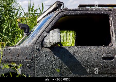 Schwarzer SUV mit einem schmutzigen Sumpfauto bedeckt, das auf dem Weg zum Angeln und zur Reise durch die Naturschutzgebiete in der Nähe von dri im Schilf des Sees festsitzt Stockfoto