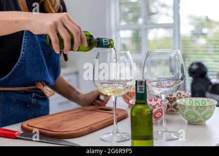 Frau in der Küche gießt zwei Gläser Weißwein, während sie kocht Stockfoto