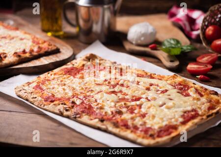 Rechteckige Form hausgemachte Pizza auf rustikalem Tisch mit Mozarella-Tomaten und Basilikum aus der Nähe Stockfoto