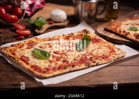 Rechteckige Form hausgemachte Pizza auf rustikalem Tisch mit Mozarella-Tomaten und Basilikum aus der Nähe Stockfoto