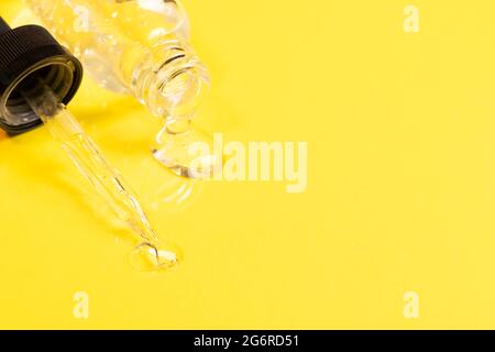 Kosmetisches flüssiges Gel-Serum-Gleitmittel fließt aus der Glasflasche Tropferflasche auf gelbem Hintergrund. Gesichts- und Körperpflege Stockfoto