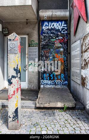 Graffiti-bedecktes Wandfragment und DDR-Nationalwappen auf dem Postweg vor dem Checkpoint Charlie Museum in Mitte, Berlin, Deutschland Stockfoto