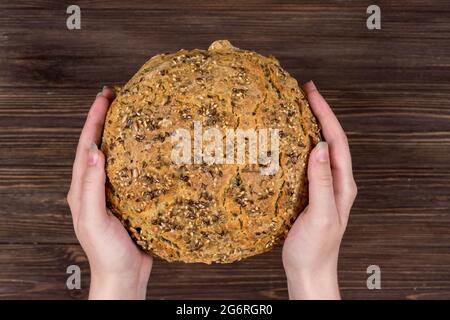 Nahaufnahme weiblicher Hände auf einem dunklen Holztisch mit frischem Brot, Draufsicht. Hausgemachtes, hefefreies Brot mit Chiasamen, Leinsamen, Sonnenblumenkernen Stockfoto