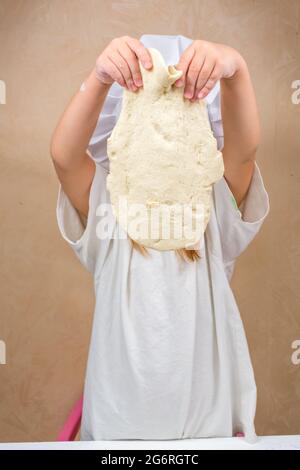 Ein kleines Mädchen hält den Teig nach Gewicht, bedeckt ihr Gesicht. Die Entwicklung der Feinmotorik bei Kindern. Salzteig modellieren. Stockfoto