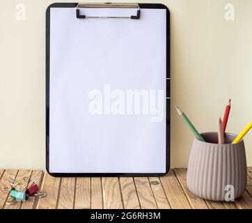 Plain Office Clipboard mit einem Stapel von Stifte in EINEM Halter auf einem Tisch. Leeres Papierblatt mit bunten Bleistiften Behälter auf EINEM Schreibtisch platziert. Stockfoto