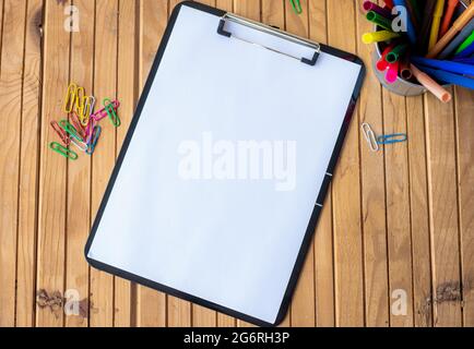 Plain Office Clipboard mit einem Stapel von Stifte in EINEM Halter auf einem Tisch. Leeres Papierblatt mit bunten Bleistiften Behälter auf EINEM Schreibtisch platziert. Stockfoto