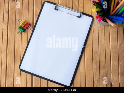 Plain Office Clipboard mit einem Stapel von Stifte in EINEM Halter auf einem Tisch. Leeres Papierblatt mit bunten Bleistiften Behälter auf EINEM Schreibtisch platziert. Stockfoto
