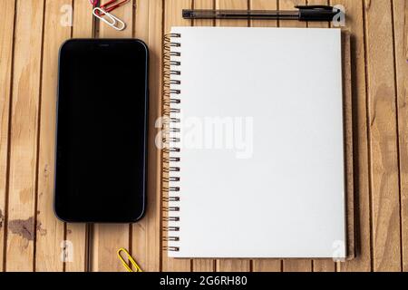 Leeres Geöffnetes Journal Neben Mobile Mit Stifte Auf Holzschreibtisch. Leeres Spiral Notebook Pad neben EINEM Telefon mit Kugelschreibern auf EINEM Tisch. Stockfoto