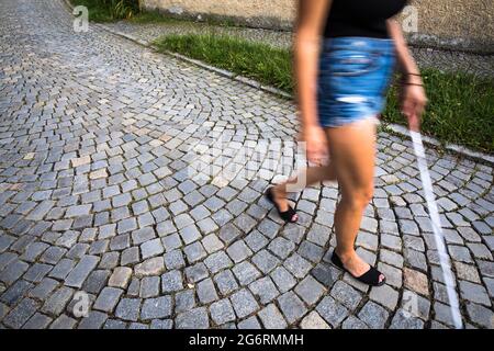 Blinde Frau, die auf den Straßen der Stadt geht, mit ihrem weißen Stock, um den städtischen Raum besser zu navigieren und sicher an ihr Ziel zu gelangen Stockfoto