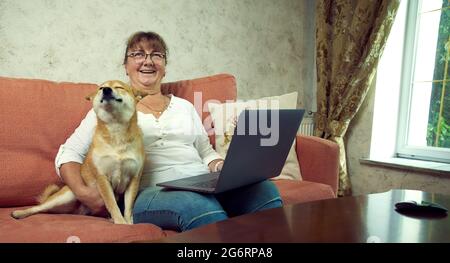 Lächelnde Frau und Hund sitzen auf dem Sofa beim computerю Closeup-Foto. Stockfoto