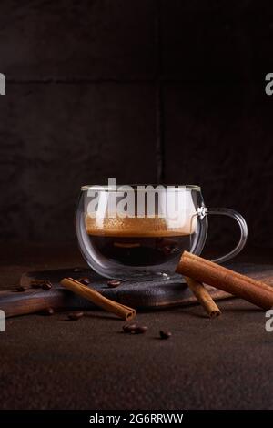 Heißer und aromatischer Kaffee, der aus der Glastasse auf dem dunklen Hintergrund ausläuft. Konzept von leckeren Erfrischungsgetränken mit Kaffee. Platz für Text kopieren, Menü o Stockfoto