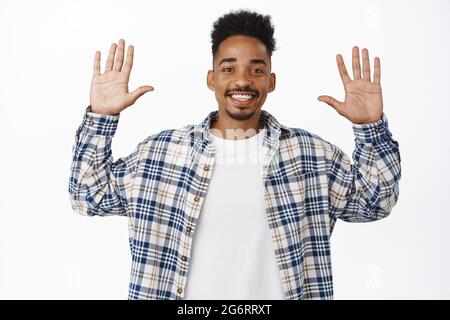Bild eines gutaussehenden, freundlich aussehenden jungen Mannes, der sich verabschiedet. afroamerikanischer Typ lächelt weiße Zähne, hebt die Arme, zeigt leere Hände, steht darüber Stockfoto
