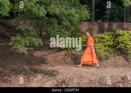 Ein junger buddhistischer Mönch mit traditionellen Safranroben, der am Chao Phraya Flussufer in Bangkok in Thailand in Südostasien entlang läuft. Stockfoto