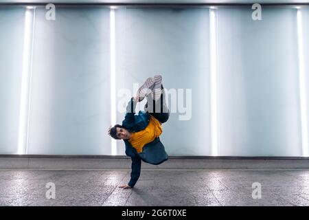 Talentierter junger Mann, der mit Lichtern gegen die weiße Wand tanzt und Breakdance übt. Stockfoto