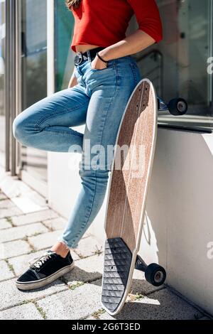 Unbekanntes Mädchen, das auf der Straße neben ihrem braunen Longboard steht. Stockfoto