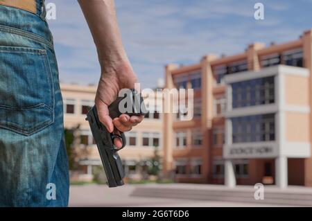 Konzept der Pistolensteuerung. Ein junger bewaffneter Mann hält an einem öffentlichen Platz in der Nähe der High School eine Pistole in der Hand. Stockfoto