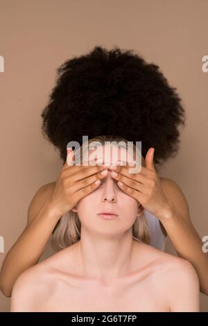 Eine dunkelhaarige Frau, die die Augen vor einer blonden Frau schließt Stockfoto