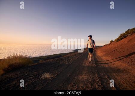 Mann genießen Blick über Wolken. Junger Wanderer, der bei Sonnenuntergang auf unbefestigterem Weg gegen die Landschaft geht.Teneriffa, Kanarische Inseln, Spanien. Stockfoto
