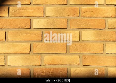 Der Schatten des Baumes fällt auf die Steinmauer. An einer Steinmauer aus Lehmstein ein Schatten an einem sonnigen Tag Stockfoto