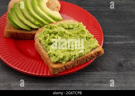 Avocado Toast auf einem roten Teller auf einem rustikalen Holztisch Stockfoto