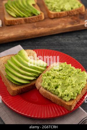 Avocado Toast auf einem roten Teller auf einem rustikalen Holztisch Stockfoto