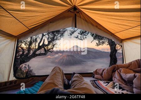 Reisender Mann entspannen und den Blick auf Bromo aktiven Vulkan in einem Zelt am Morgen im Bromo Tengger Semeru Nationalpark, Indonesien Stockfoto