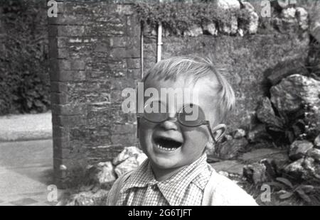 1960, historisch, ein kleiner Junge mit einem lugh, der seine Schwestern mit grooviger Sonnenbrille auf dem Kopf trägt, England, Großbritannien. Stockfoto