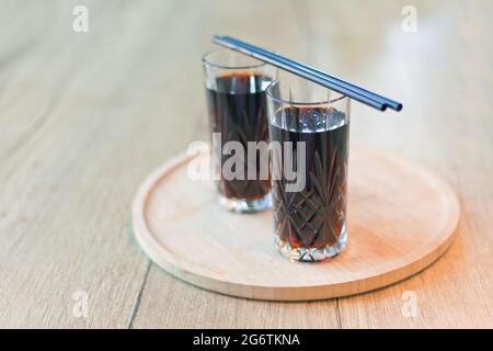 Schwarzes Getränk mit Trinkhalmen. Zwei Gläser Cuba Libre oder Long Island Eistee Cocktail mit einer Cola, Eis, Limette, Rum mit Trinkhalmen auf Holztisch mit Blick t Stockfoto