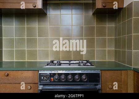 Das Innere einer alten Retro-Vintage-Küche mit antikem Ofen mit braunen Holzschränken, grünen Stilfliesen der alten Schule, muss renoviert werden Stockfoto