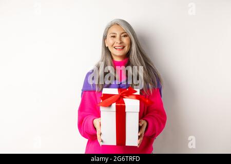 Schöne asiatische ältere Frau lächelnd, gratulierend mit Valentinstag, halten Geschenk in der Box, stehend über weißem Hintergrund Stockfoto
