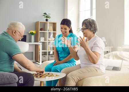 Glückliches Rentnerehepaar und ihre Krankenschwester spielen Dame und Spaß zusammen haben Stockfoto