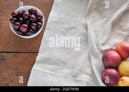 Rote und gelbe Pfirsiche liegen auf einer Leinentischdecke. Auf einem roten Holztisch liegen rote Kirschen in einer weißen Schale. Stockfoto