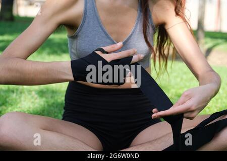 Nicht erkennbar keine binäre Person, die muay thai-Handpackungen trägt, sitzt auf Gras in einem Park. Sport im Freien. Stockfoto
