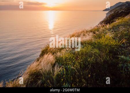 Luftaufnahme der Sommerküste mit Gras und ruhigem Meer. Küstenlinie mit Sonnenuntergangsfarben Stockfoto