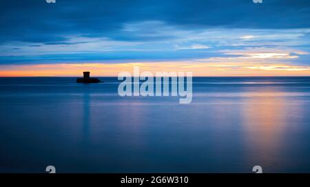 Bild des Rocco Tower in St Ouens Bay, Jersey CI bei Sonnenuntergang mit seidigen Wasser dunklen Wolken mit Spiegelung der Sonne. Stockfoto