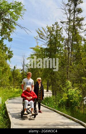 Großmutter, Tochter und ihr Sohn genießen einen Spaziergang in einem Naturgebiet mit Promenade, Enkel schieben Rollstuhl für die Mobilität, Baileys Harbor, WI, USA Stockfoto