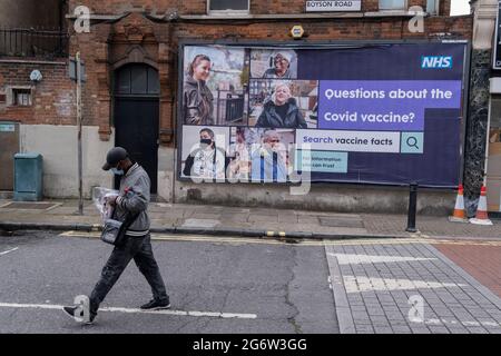 Ein im Süden Londoners getragener Bürger, der ein Gesicht trägt und an einer Plakatwand des staatlichen Gesundheitsdienstes vorbeigeht, die einen Link für offizielle Informationen über Covid-Impfstoffe enthält, Ein Versuch, Fehlinformationen und Verschwörungstheorien der Öffentlichkeit in Lambeth - einem Stadtteil, in dem es hohe Infektionsraten von Covid- und Delta-Varianten gab - am 6. Juli 2021 in Camberwell, London, England entgegenzuwirken. Stockfoto
