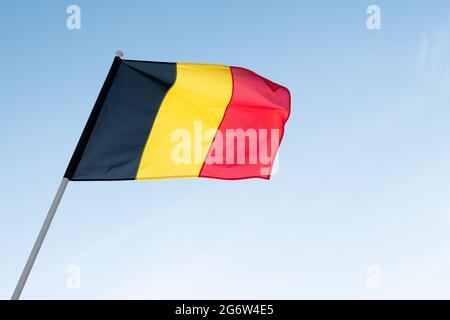 Flagge Belgiens auf blauem Himmel Hintergrund. Belgische Flagge winkt im Wind Stockfoto