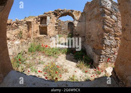 Rote Mohnblumen wachsen innerhalb der Steinmauern und Bögen einer alten griechischen Ruine im Inneren der Insel Mykonos Stockfoto
