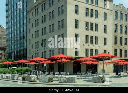 New York, NY - USA - 6. Juli 2021: Landschaftsansicht eines öffentlichen Platzes mit roten Sonnenschirmen im angesagten Meatpacking District an der Kreuzung o Stockfoto