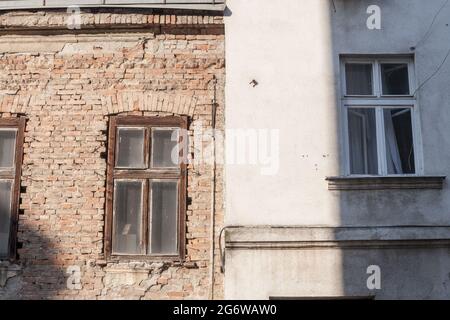 Bild von zwei Fassaden, nebeneinander, eine in rauem und rohem beschädigten roten Ziegel, die andere mit einer weißen Betondichtung. Stockfoto