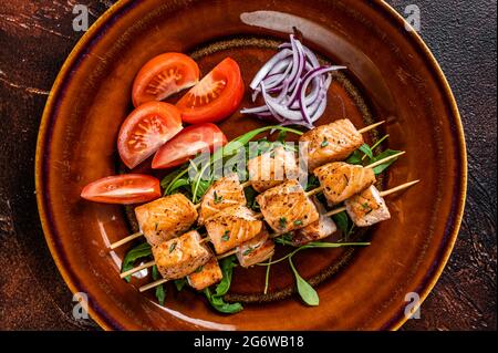 Barbecue Lachs Kebab Spieße auf rustikalem Teller mit Gemüse. Dunkler Hintergrund. Draufsicht Stockfoto