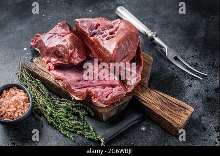 Rohes geschnittes Rind- oder Kalbsherz auf einem Schlachtbrett. Schwarzer Hintergrund. Draufsicht Stockfoto