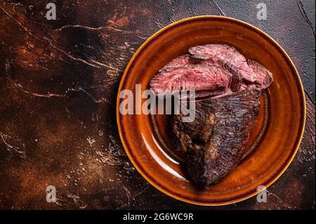 Gerösteter Aufhänger oder Onglet-Rinderfleischsteak in Scheiben auf einem rustikalen Teller mit Hackschnitzel. Dunkler Holzhintergrund. Draufsicht. Speicherplatz kopieren Stockfoto